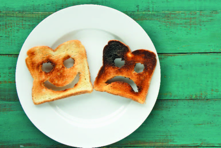 A piece of toast with a smile cut out and another slightly darker piece of toast with a frown cut out